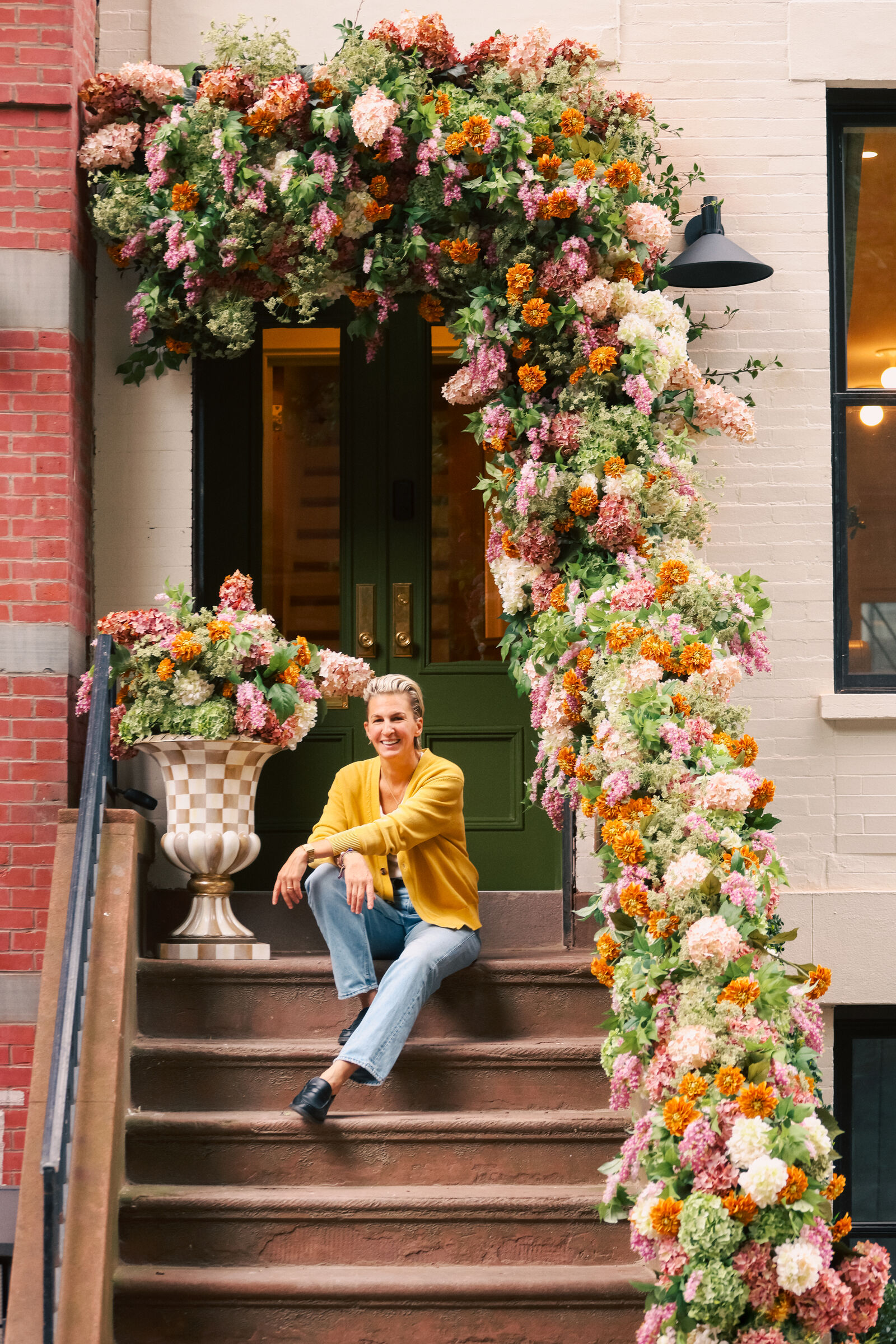 Albi Zhubi seated on a brownstone stoop under an arch of flowers