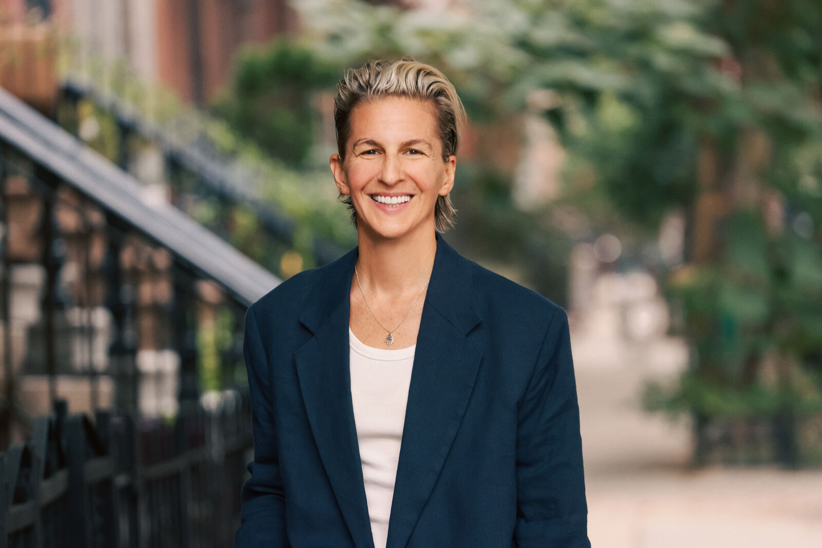 Albi Zhubi in a navy blazer and white top, smiling on a Brooklyn street